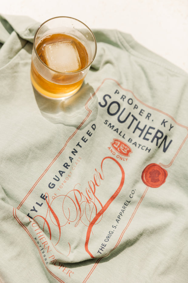 A Small Batch SS Tee t-shirt with a glass of bourbon next to it.