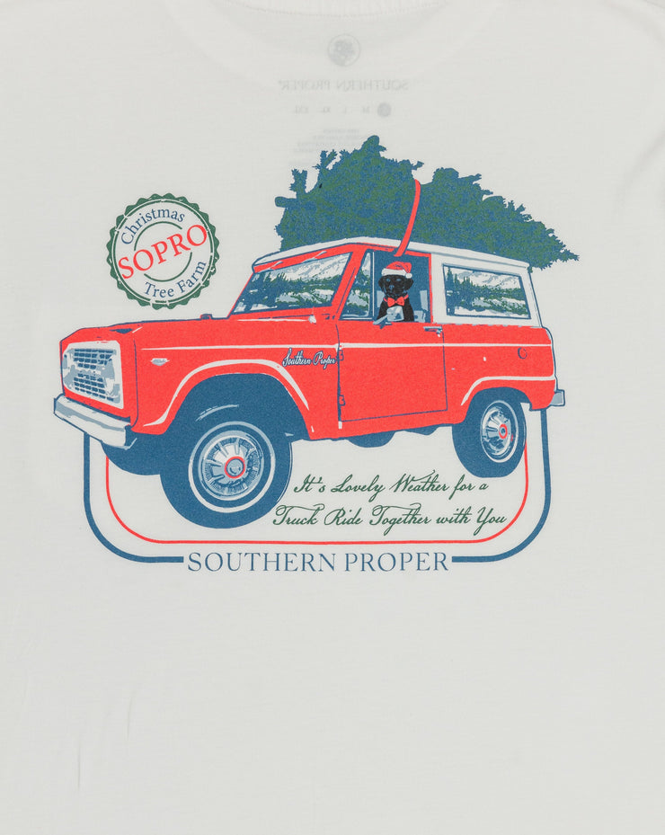 A Lovely Weather LS Tee: White with a printed logo of a red truck carrying a Christmas tree, made from Peruvian cotton.