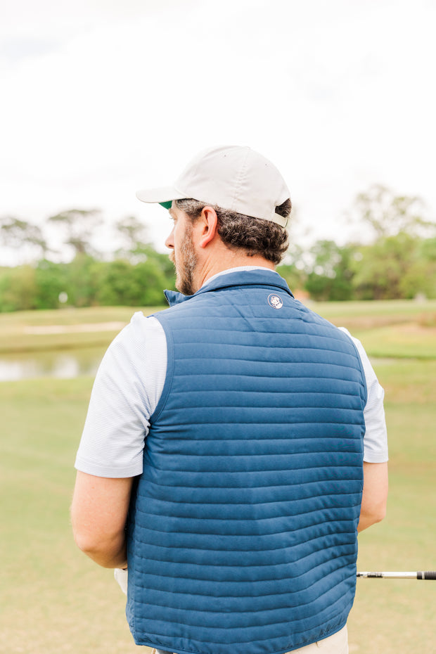 A man wearing a Quilted Field Vest is seen standing on a golf course, ready to showcase his golf swing.