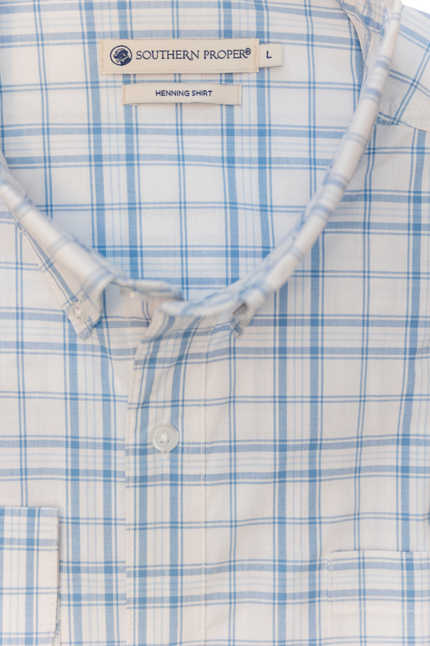Close-up of a neatly folded Royal woven shirt in Coastal Blue and white plaid, featuring a label that reads "Southern Proper" and "Henning Shirt, L." This shirt combines a Tailored Fit with classic design and modern style.