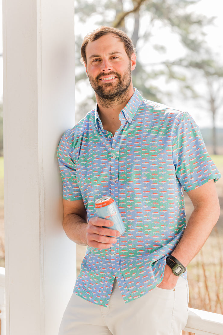A man is standing on a porch holding a Mangrove cocktail shirt.
