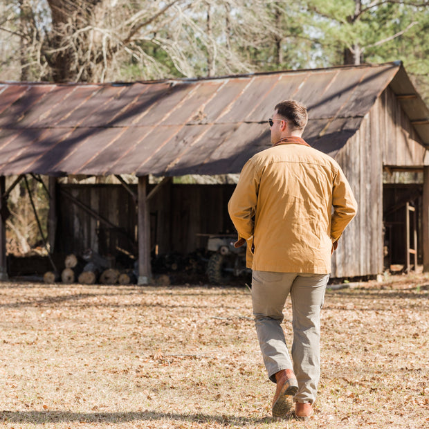 A man wearing a Bluff Barn Jacket is walking in front of a barn.