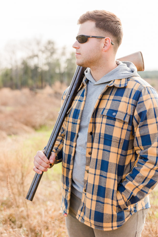 A man in a Southern Shacket holding a shotgun in a field.