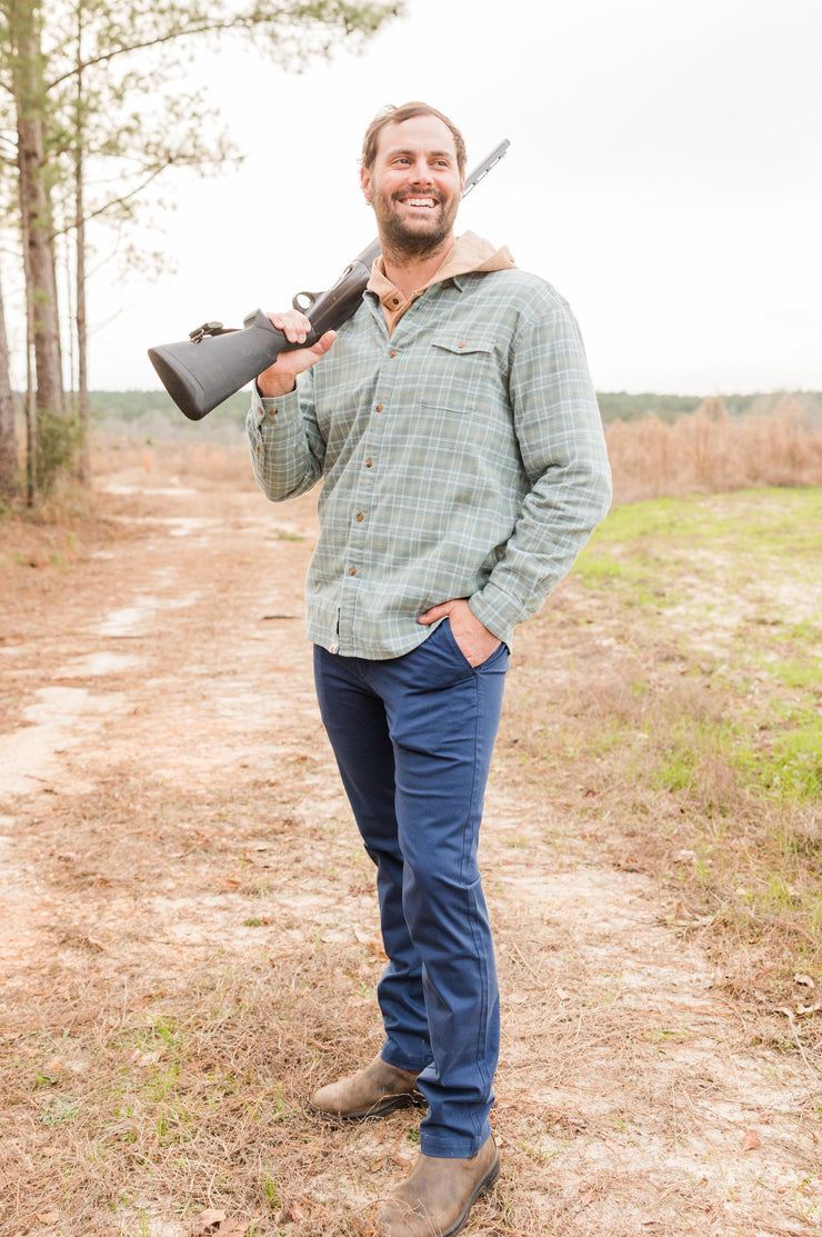A man, dressed in a tailored fit Thomasville pant, is holding a rifle on a dirt road in Thomasville.